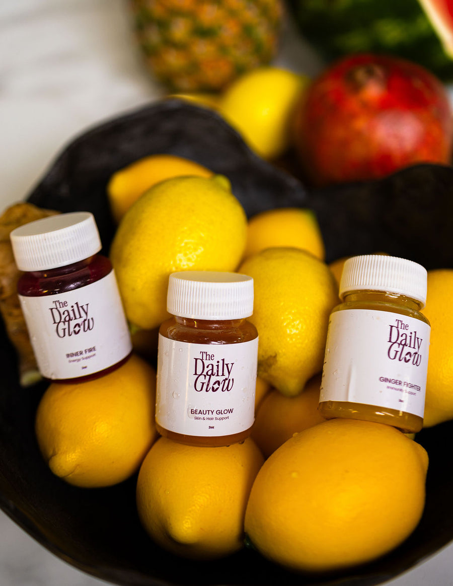 A fresh lineup of The Daily Glow cold pressed juices and wellness shots surrounded by whole fruit